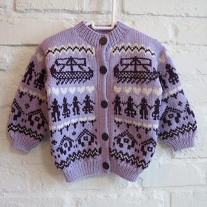 Op de afbeelding: Een lavendelkleurig gebreid vest met een ronde hals en donkerbruine knopen. De trui heeft een herhalend patroon van boten, mensen, huizen en harten in donkerpaars en crème. Het vest wordt op een witte hanger getoond.