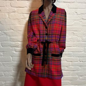 May include: A long-sleeved jacket featuring a vibrant red, blue, and green plaid pattern. The garment includes a black velvet collar, black velvet cuffs, and a black velvet tie at the waist. It has a button-down front and two front pockets.