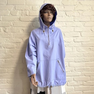 May include: A light purple hooded pullover jacket featuring a half-zip front closure with a metallic zip, long sleeves, and two slanted zipped pockets on the front. The hood includes a drawstring with metallic toggles, and the hem is adjustable.