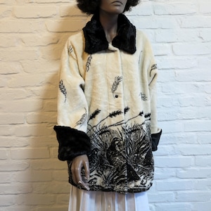 May include: Cream-colored coat with black fur collar, cuffs, and decorative elements. The coat features a button-up front and a detailed black and white graphic of birds and foliage across the lower portion.