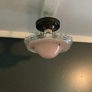 May include: A ceiling-mounted light fixture featuring a dark brown circular base and a central pale pink glass bowl. The bowl is surrounded by a clear, scalloped glass rim with a textured, ribbed pattern, secured by small metal hardware.