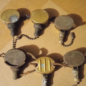 以下が含まれることがあります： 真鍮と金属製のヴィンテージな天井ファン用プルチェーン6個セット。チェーンは互いに接続されており、装飾的なデザインが施されています。