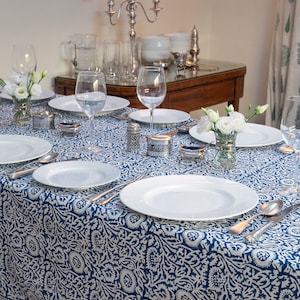 May include: A white tablecloth with a blue and white floral pattern, set for a dinner party. The table is decorated with white flowers in small vases and silver serving pieces.