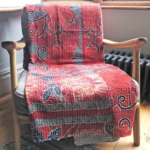 May include: A red and black kantha quilt with a floral pattern draped over a wooden chair.