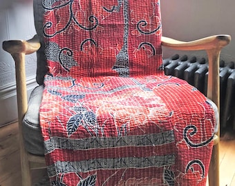 May include: A red and black kantha quilt with a floral pattern draped over a wooden chair.