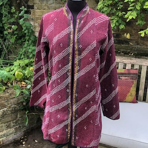 May include: A burgundy quilted jacket with a white and gray geometric pattern. The jacket has a mandarin collar and a gold and purple trim.