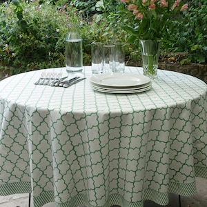 May include: A white round tablecloth with a green geometric pattern. The tablecloth has a green and white striped border. The tablecloth is set with white plates, silverware, and glasses.