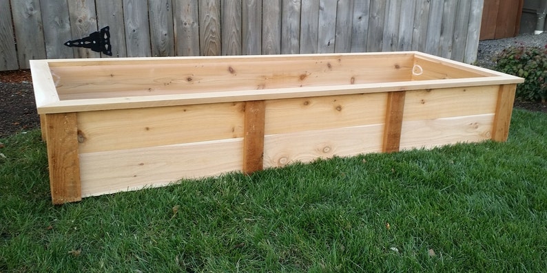 May include: A rectangular wooden raised garden bed made of cedar planks. The bed is sitting on a green lawn.