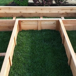 May include: A wooden raised garden bed with three sections. The bed is filled with green grass.