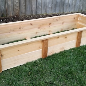May include: A wooden raised garden bed made of cedar planks. The bed is empty and ready for planting.