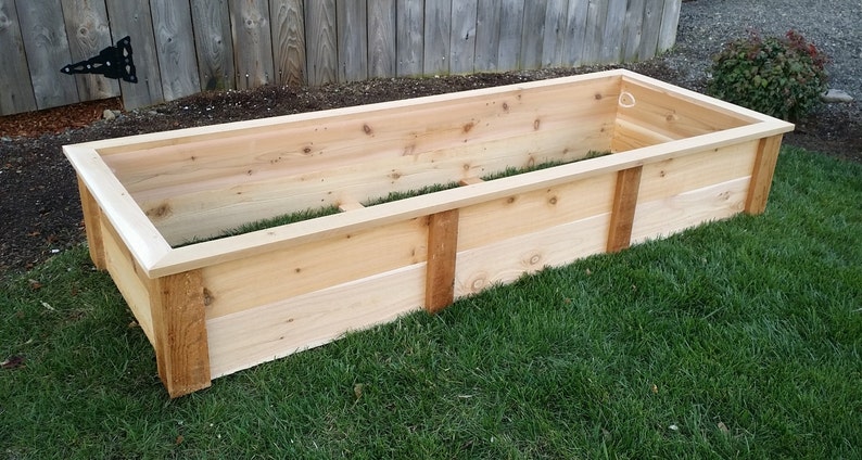 May include: A wooden raised garden bed made of cedar planks. The bed is empty and ready for planting.