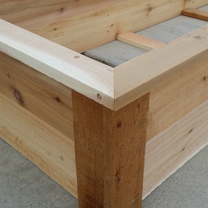 May include: Close-up of a wooden planter box corner, showing the mitered joints and natural wood grain. The box is made of unfinished cedar wood.
