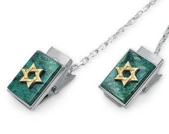May include: A pair of silver tone tie clips with a green stone and gold star of David design. The clips are connected by a silver chain.