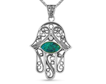 May include: A silver necklace with a hamsa hand pendant featuring a turquoise blue eye in the center. The pendant is intricately detailed with filigree work.