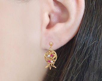 May include: Gold dangle earrings with a pomegranate design featuring red and white gemstones.
