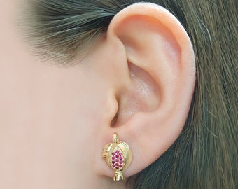 May include: Gold-toned earrings shaped like a pomegranate with red cubic zirconia stones.