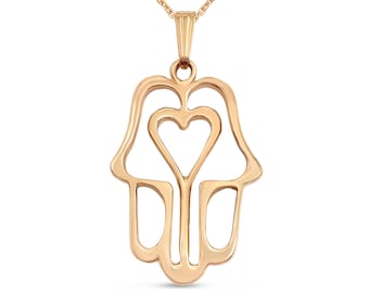 Puede incluir: Un collar dorado con un colgante de mano de hamsa con un corazón recortado. El colgante es un diseño delicado y calado.