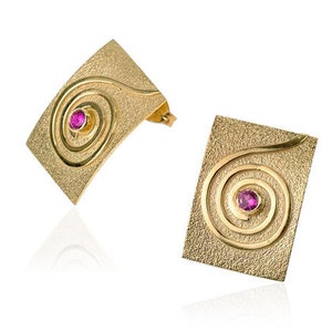 May include: A pair of gold earrings with a textured finish. Each earring features a square-shaped design with a spiral pattern and a small pink gemstone in the center.