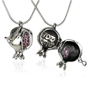 May include: A silver necklace with a pomegranate pendant that opens to reveal a small compartment. The pomegranate is decorated with red gemstones and Hebrew writing.