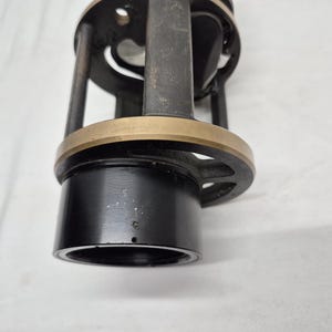 May include: A cylindrical black metal fishing reel component featuring a brass-colored circular ring, vertical support struts, and an open frame design. The base consists of a smooth black tube, while the upper section includes a circular plate.