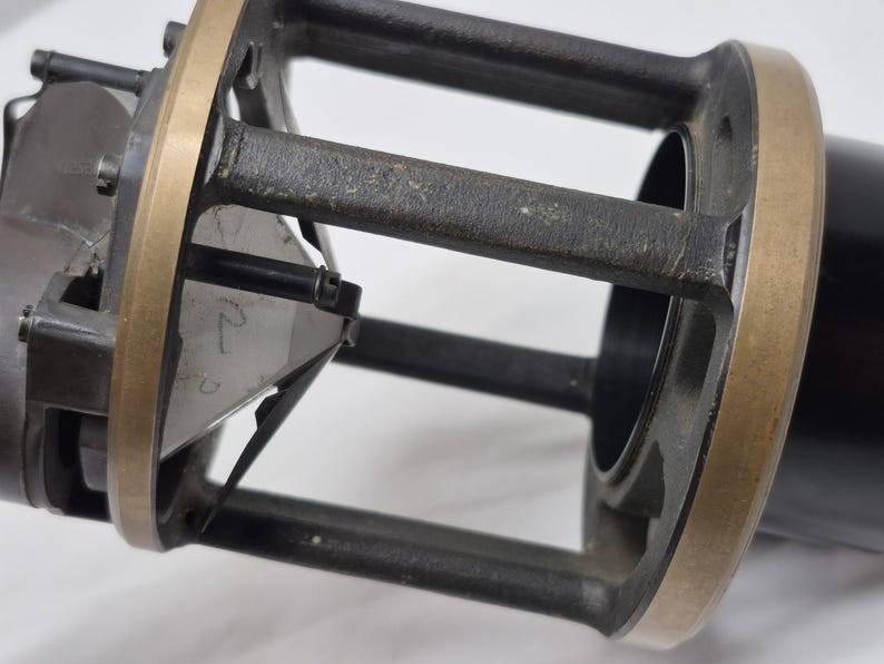 May include: A mechanical device featuring a cylindrical black housing with a brass-colored metal frame. The structure includes vertical supports and a central triangular component with the handwritten number 2 visible on its surface.