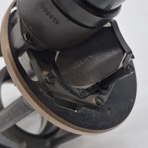 May include: A mechanical component featuring a dark gray cylindrical housing with the number 418509 engraved on the side. It includes a circular brass-toned rim, a central dark metal plate with the word VIFSED stamped on it, and small screws.