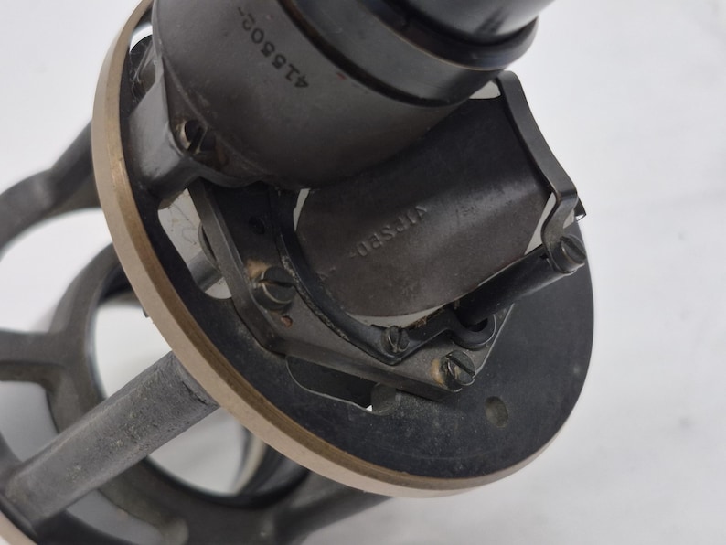 May include: A mechanical component featuring a dark gray cylindrical housing with the number 418509 engraved on the side. It includes a circular brass-toned rim, a central dark metal plate with the word VIFSED stamped on it, and small screws.
