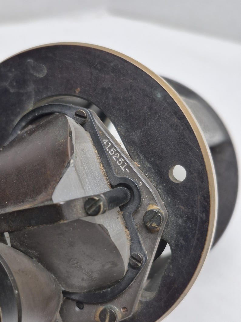 May include: A mechanical component featuring a circular black metal frame with a metallic rim. A central glass prism is secured by a black bracket held with screws. The bracket is engraved with the serial number 415251. A small circular hole is visible on the right side of the frame.
