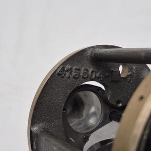 May include: A dark gray cast metal component featuring a circular frame with the embossed number 415604-1. The object includes a central opening with visible internal glass elements and a smooth, metallic outer edge, showing industrial construction.