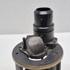 May include: A black cylindrical optical component featuring a vertical tube and a curved, metallic reflective prism assembly mounted on a circular base. The assembly includes small screws and engraved numerical markings on the metal surfaces.