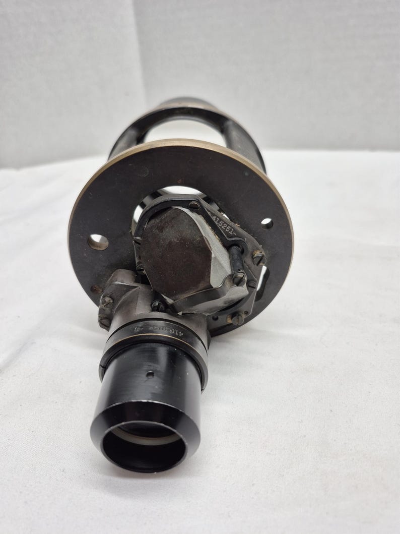 May include: A black metal optical instrument component featuring a circular mounting plate with two holes, a central glass prism assembly, and a cylindrical lens barrel. The metal frame displays the engraved serial number 415251 on the prism housing.
