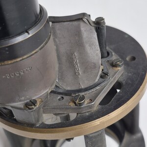 May include: A black and metallic mechanical device featuring a cylindrical component with the number 415502 engraved on the side. A curved metal plate attached to the frame displays the stamped text 412520, secured by small screws on a circular base.