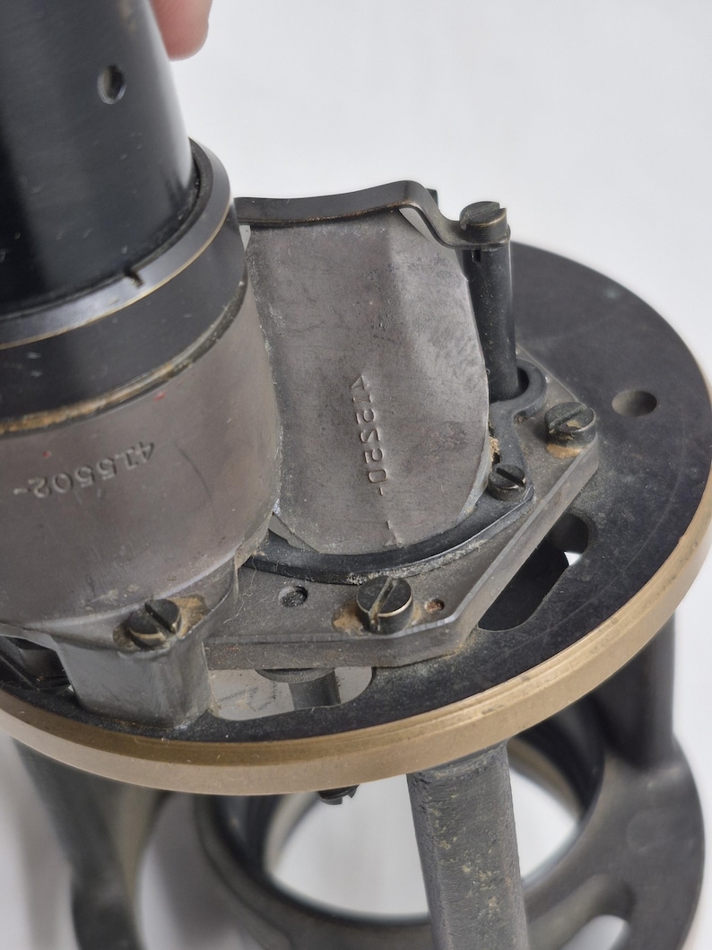 May include: A black and metallic mechanical device featuring a cylindrical component with the number 415502 engraved on the side. A curved metal plate attached to the frame displays the stamped text 412520, secured by small screws on a circular base.