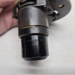 May include: A cylindrical black metal mechanical component featuring a brass-colored top flange and a series of small circular indentations. The side of the lower section is clearly stamped with the alphanumeric text 415505-1 in a clean, sans-serif font.