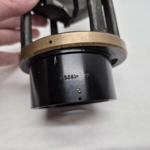 May include: A cylindrical black metal component featuring a brass-colored ring at the top and vertical support struts. The black base displays the engraved text 415261-2, along with small circular holes and a tiny metal pin protruding from the surface.