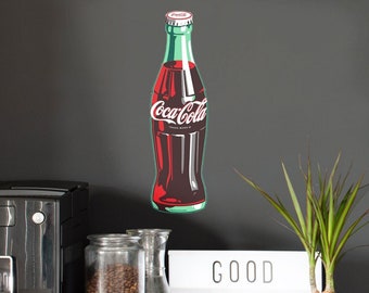 May include: A wall decal featuring a classic Coca-Cola glass bottle with a red and dark brown liquid, a white logo, and a silver cap. The design is rendered in a stylised graphic illustration with bold outlines, positioned on a dark grey wall.