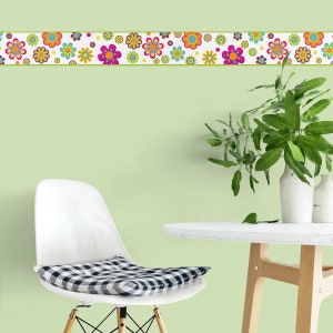 May include: A white chair with a black and white checkered cushion sits in front of a green wall with a colorful floral border. A white table with a wooden base sits in the foreground.