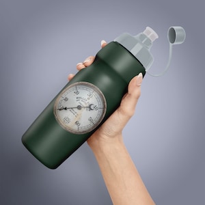 May include: Dark green water bottle with a gray cap and a vintage-style gauge. The gauge reads "Mueller Steam Hot Water Control" and displays numbers from 10 to 60. The bottle is held by a person.