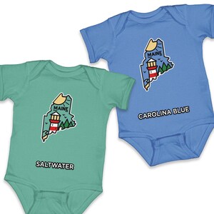 May include: Two baby onesies, one in Carolina blue and the other in a seafoam green. Each features a graphic of the state of Maine with a lighthouse and the text "MAINE". The blue onesie has "CAROLINA BLUE" text, and the green one has "SALTWATER".