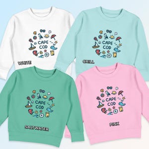 May include: Four sweatshirts in different colors: white, light blue, light green, and pink. Each sweatshirt features a circular design with the text "CAPE COD" and various beach-themed icons, including a seagull, an umbrella, a beach ball, a seashell, a lighthouse, and a whale.