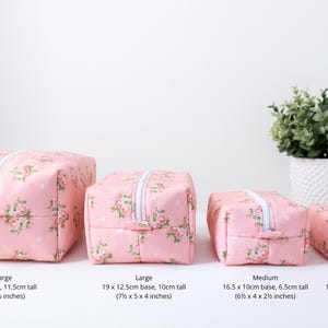 May include: Four rectangular pink pouches with a floral pattern and white polka dots, featuring white zippers. Sizes include: Extra Large 8.5 x 6 x 4.5 inches, Large 7.5 x 5 x 4 inches, Medium 6.5 x 4 x 2.5 inches, and Small 5 x 2.5 x 2 inches.