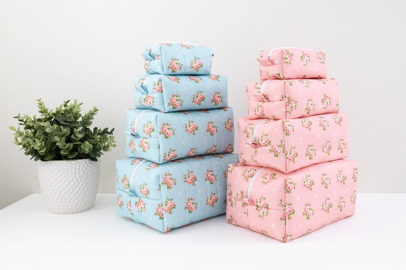 May include: A set of four light blue rectangular zippered pouches and four light pink rectangular zippered pouches, all featuring a white polka dot pattern and a floral print of small pink roses with green leaves, stacked in two separate columns.
