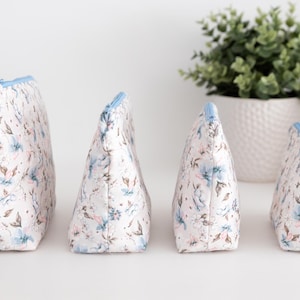 Four floral zip pouches standing upright in a row, showing the flat boxed bottom and depth.
