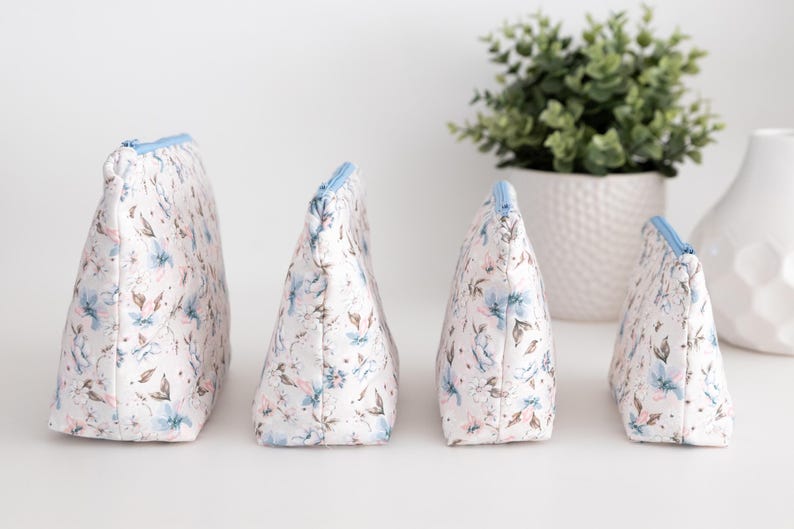 Four floral zip pouches standing upright in a row, showing the flat boxed bottom and depth.