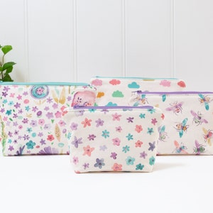 May include: Four zippered pouches with different floral and bee patterns. The pouches are made of white fabric with a light blue zipper and a purple zipper pull.