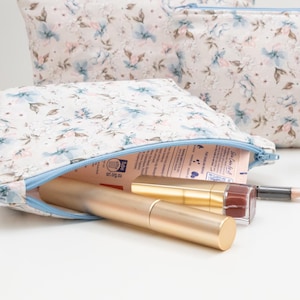 Floral zip pouch opened on a table and filled with makeup and lip products, showing everyday use and size.