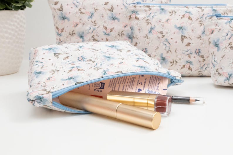 Floral zip pouch opened on a table and filled with makeup and lip products, showing everyday use and size.