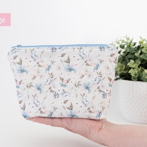 Large floral zip pouch held in one hand beside a potted plant, labelled Large.