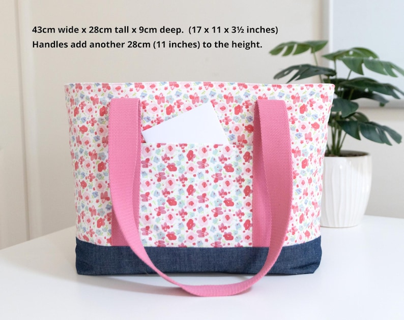 Puede incluir: Un bolso tote con estampado floral en rosa, rojo y azul, con una base de mezclilla azul oscuro y asas de tela rosa. Mide 43 cm de ancho por 28 cm de alto y 9 cm de profundidad, con asas que a&ntilde;aden otros 28 cm a la altura total.