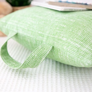 Puede incluir: Una almohada verde con un patr&oacute;n blanco y un asa. La almohada est&aacute; hecha de una tela suave y texturizada.